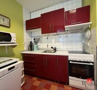 A kitchen in a studio apartment with red cabinets and white appliances.