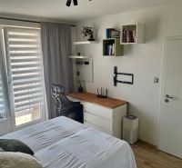 Bedroom in a 2-room apartment with a work corner, bed, and wooden decor on the floor.