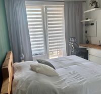 Bedroom in a 2-room apartment with a desk and large windows.