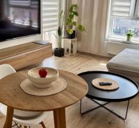 Bright living room in a 2-room apartment with a TV, window, and tables. Floor with wood decor.