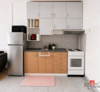 A kitchen in a 2-room apartment with appliances and a wooden decor floor.