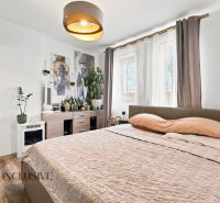 Bedroom with light walls, a bed, and decorations, floor with wooden decor.