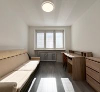 A room in a 3-room apartment with a sofa, a desk, and a wooden decor floor.