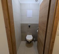 A toilet in a 2-room apartment with ceramic tiles and a wooden decor floor.