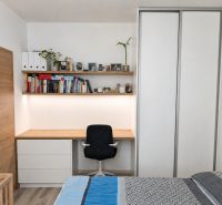 A bedroom in a two-room apartment with a work corner, books, and a floor with a wooden decor.