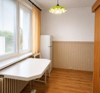 A kitchen in a 2-room apartment with a table, chair, refrigerator, and a floor with a wooden decor.