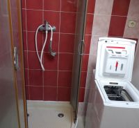 A shower enclosure in the bathroom of a 2-room apartment, with a washing machine installed.
