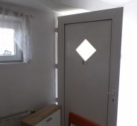 The entrance door in a 2-room apartment with a wooden decor of the dresser and chair.