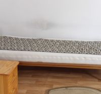 A bed in a room with a wood-patterned floor, next to a wooden cabinet.
