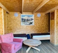 A room in a family house with two beds, a pink armchair, and a wooden-patterned floor.