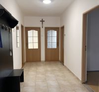 A hallway in a family house with tiles, wooden doors, and a coat rack.