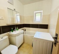 A bathroom in a family house with a bathtub, a washing machine, and a sink, with light tiles.