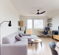 A bright living room with a sofa, TV, table, and wood-patterned flooring in a three-room apartment.