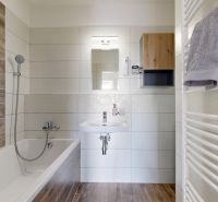 Bathroom with a bathtub, wooden decor flooring, and white tiles in a 3-room apartment.
