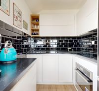 Compact kitchen in a 3-room apartment with black glossy tiles and a floor with a wood decor.