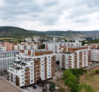 A view of apartment buildings on Nobelova Street, Bratislava - Nové Mesto, surrounded by greenery and hills.