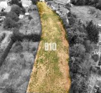 Plots - housing Kolíňany: Long plot with green grass, lined with trees and buildings.