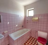 A bathroom with pink tiles and a white bathtub in a family house.