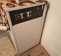 A boiler in the interior of a family house with a control panel and an orange container on top.