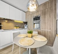 A kitchen in a 2-room apartment with a wood-patterned floor, a table, and built-in appliances.