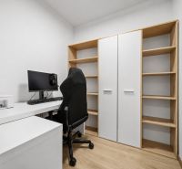 A workspace with a computer, printer, and shelves in a 2-room apartment with a wooden decor floor.