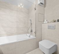 Bathroom with a bathtub and toilet in a 2-room apartment with light tiles.