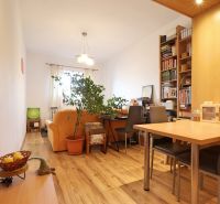 Living room with wood-patterned flooring, a sofa, a table, and a bookshelf in a two-room apartment.