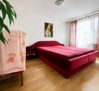 A bedroom in a family house with a red bed and a wooden decor floor.