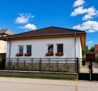 A family house in Šalgočka with a white facade, window flowers, and a hipped roof.