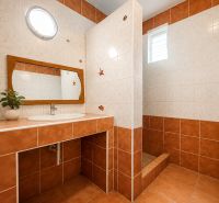 A bathroom in a family house with ceramic tiles and a wooden mirror.