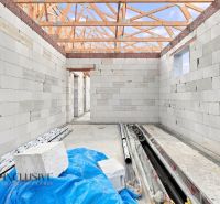 An unfinished family house in Marcelová with visible walls and a roof made of wooden beams.