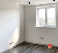 A simple room in a one-bedroom apartment with a wooden-patterned floor and white walls.
