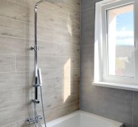 Bathroom with a bathtub and shower, wood decor tiles, large window, studio apartment.