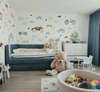 Children's room with toys, a blue bed, wallpaper with cars, and a wooden decor floor.