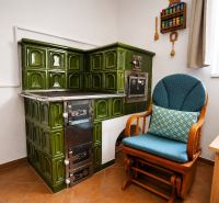 A tiled stove with green tiles next to an armchair in a family house.