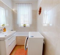 A bathroom in a 3-room apartment with a bathtub, sink, washing machine, and window.