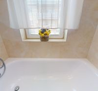 A bathroom with a shower faucet, a bathtub, and flowers on the windowsill in a three-room apartment.