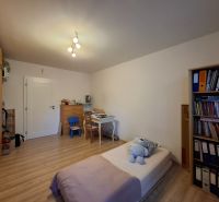 A room with a desk, a bed, and a floor with a wooden decor in a 3-room apartment.