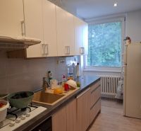 A kitchen in a 3-room apartment with a wooden decor floor and light cabinets.
