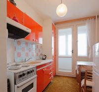 A kitchen in a 2-room apartment with orange cabinets and balcony doors.