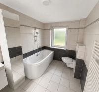 A bathroom in a family house with white sanitary ware and a bathtub, light tiles, and a radiator.