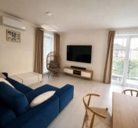 A bright living room in a family house with a blue sofa and a TV on the wall.