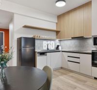 A kitchen with a dining table, appliances, and a wooden decor floor in a studio apartment.