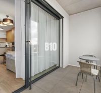 A balcony with seating and a view into a studio apartment through sliding doors.