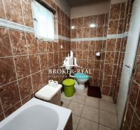 A bathroom with brown tiles, a bathtub, a toilet, and a waste bin in a family house.