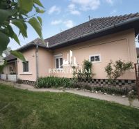 A family house in Bódvaszilas with light-colored walls, a sloping roof, and a green lawn.