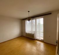 An empty room in a family house with a window, curtains, and a wooden-patterned floor.