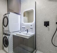 A bathroom with a washing machine, dryer, sink, illuminated mirror, and shower in a 3-room apartment.