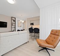 Living room in a three-room apartment with a wooden decor floor, a cream sofa, and a leather armchair.