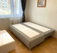 Studio apartment with a bed, wood-patterned floor, and a white table.